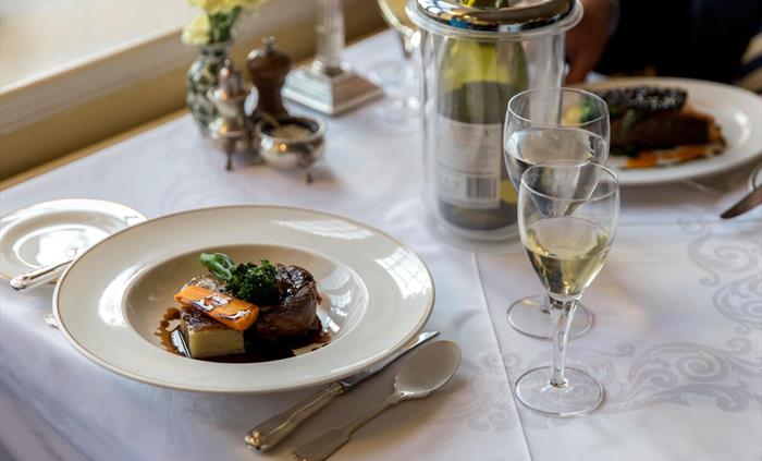 Lamb with seasonal vegetables served on dining table with wine.